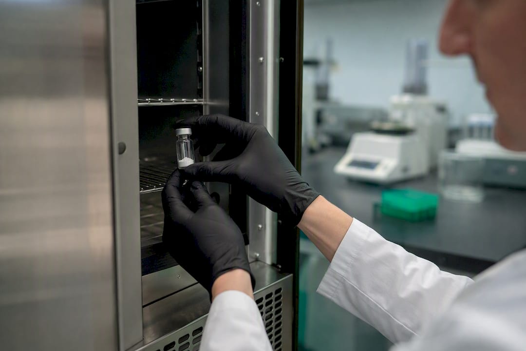Gloved hands storing peptide vial in lab